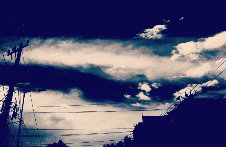 Dramatic clouds and power lines silhouetted against an intense sky